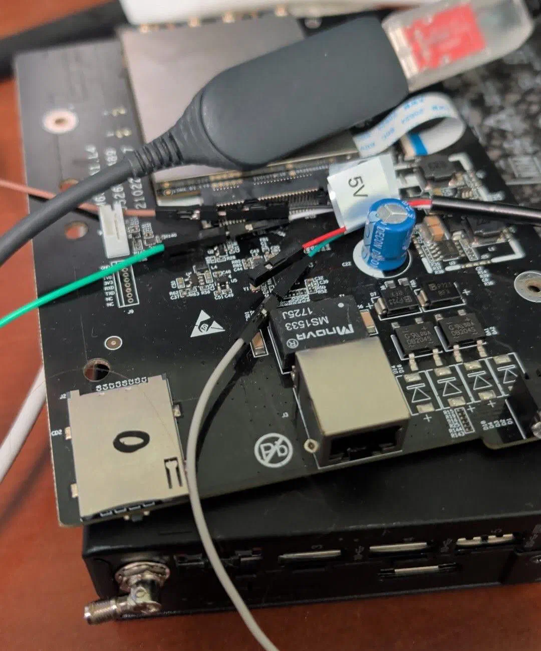 An opened Titan 4000 circuit board on a desk with jumper wires and a USB serial adapter attached