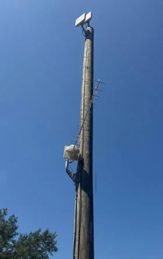 A tall wooden pole against a blue sky with two radios at the top and a Yagi antenna below